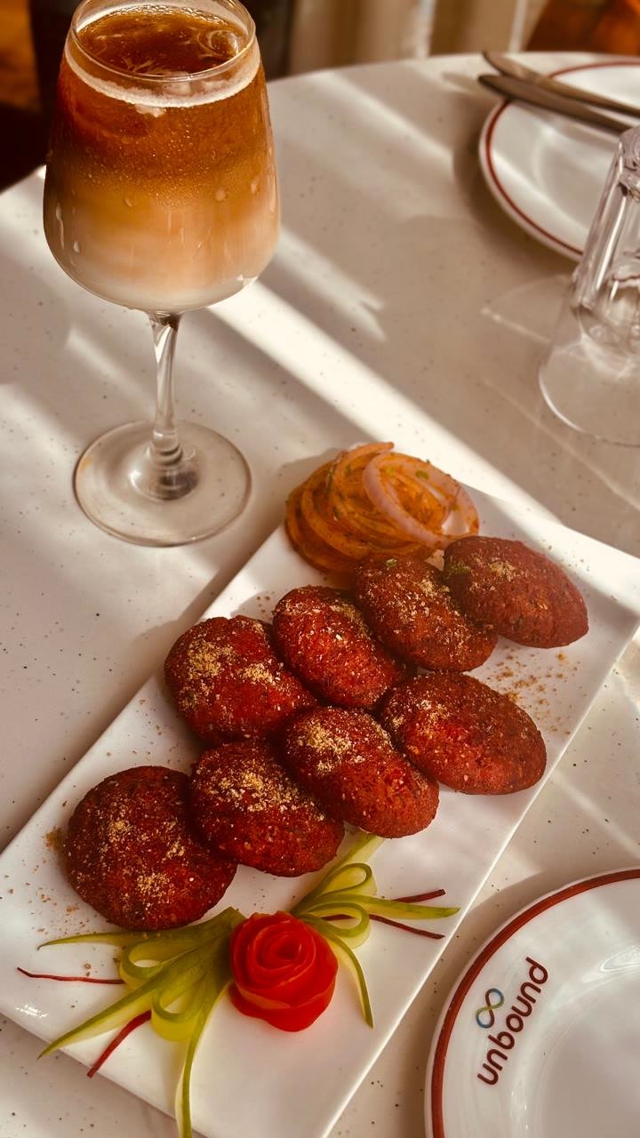 A plate of kebabs with onion rings, a cold drink in a stemmed glass beside it