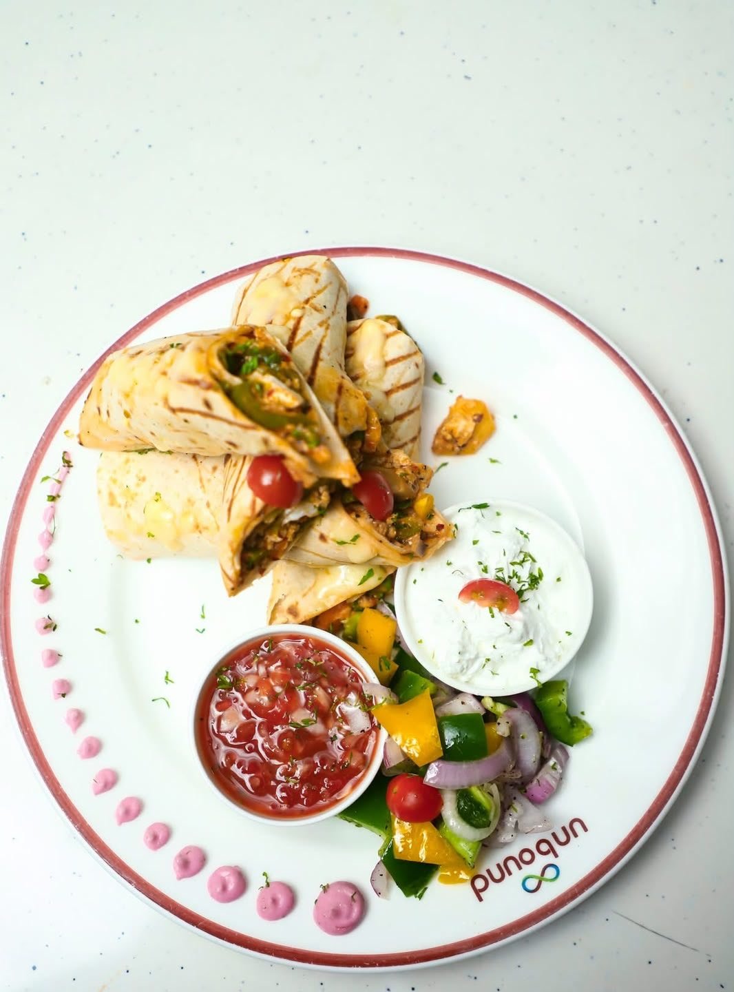 A grilled wrap cut in half, with salsa, a yoghurt dip and peppers, seen from above